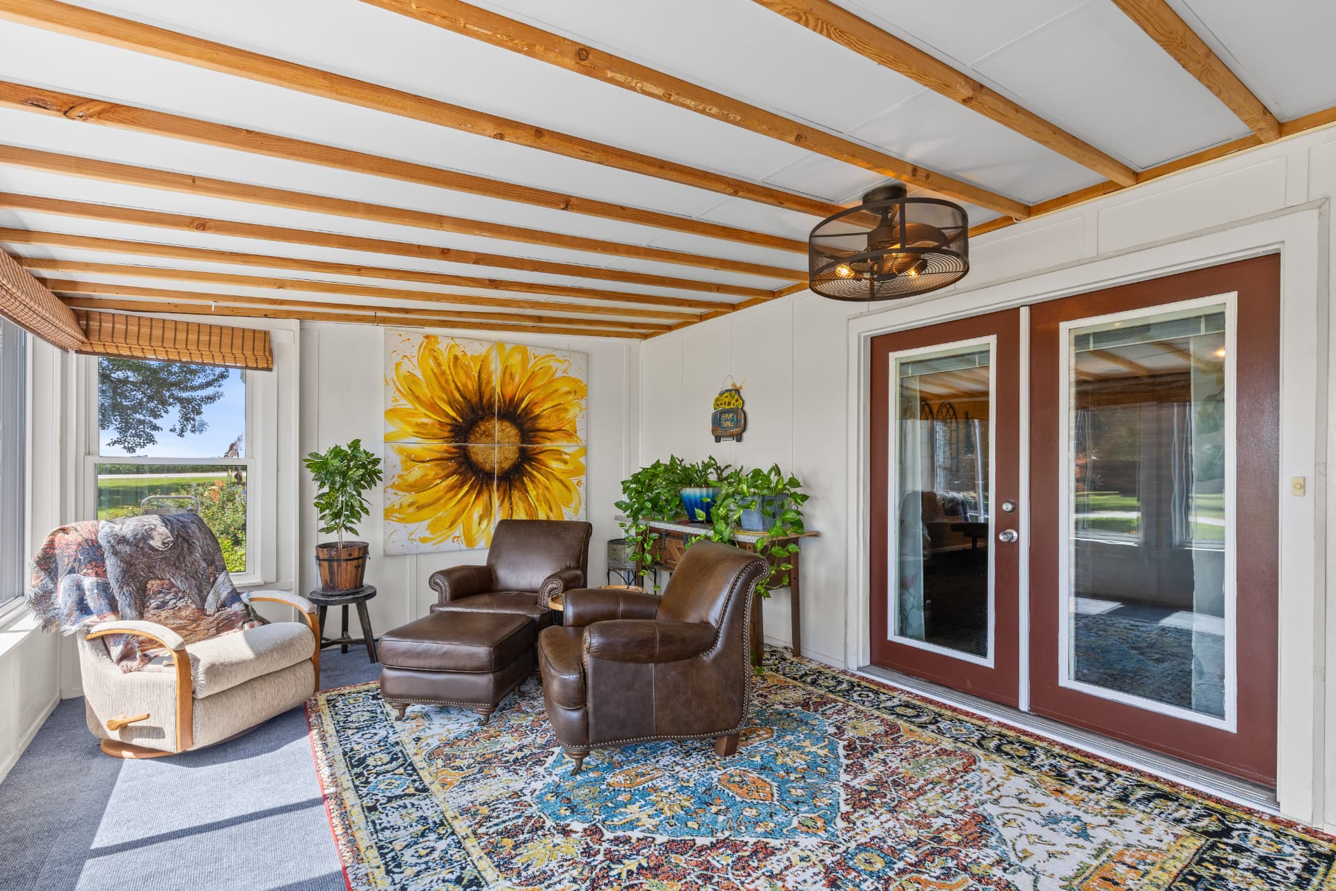 Sun porch with exposed beam ceiling, sunflower painting and French doors to the great room