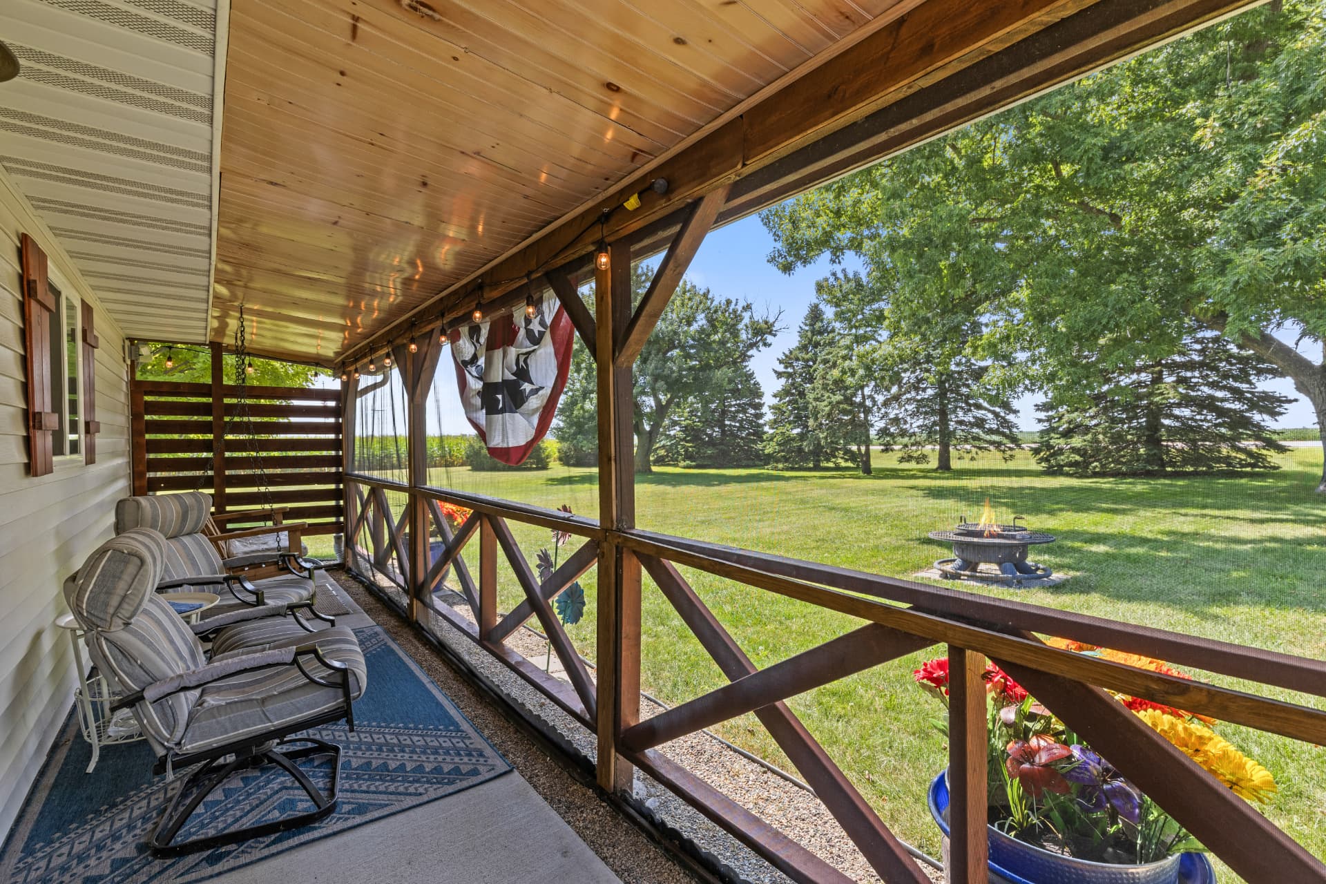 Screened-in porch with swing, patio seating and a view of the fire pit and oak trees