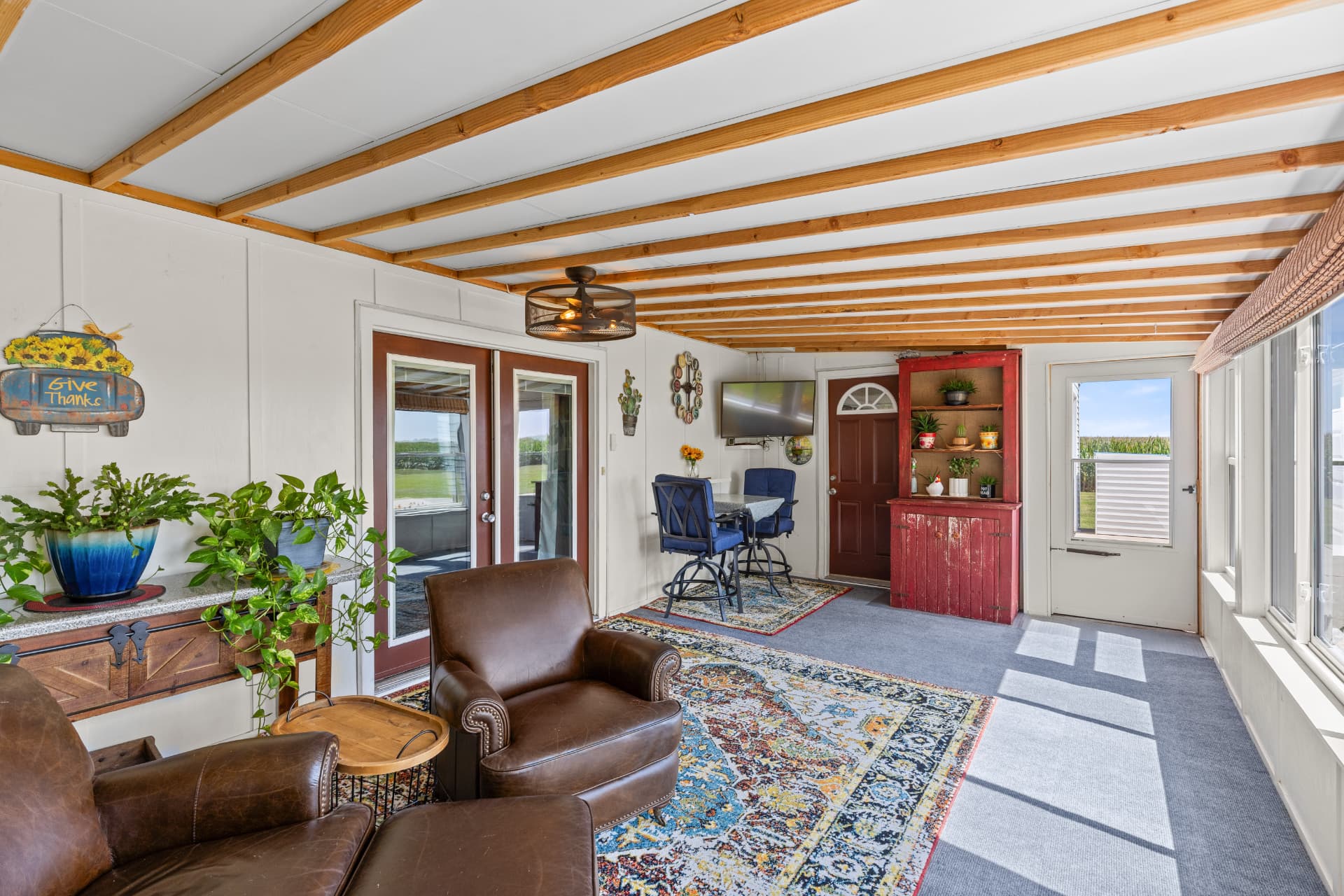 Sun porch looking toward the entry door, red cabinet and bistro table under exposed beams