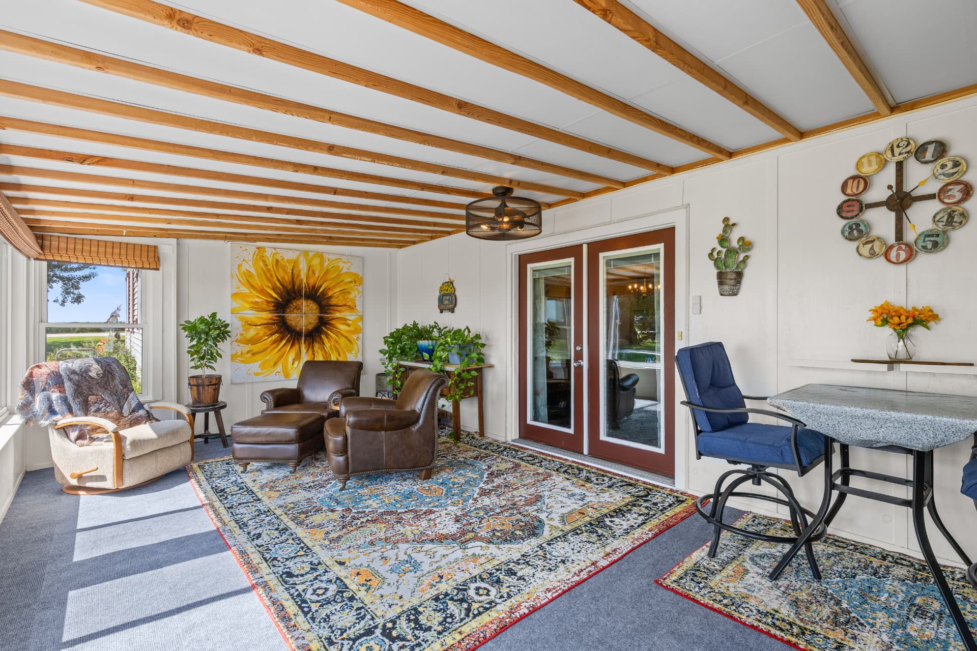 Sun porch seating area with leather chairs, sunflower art and French doors into the house